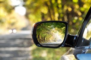 Reflection of sunny autumn road at the car side mirror.