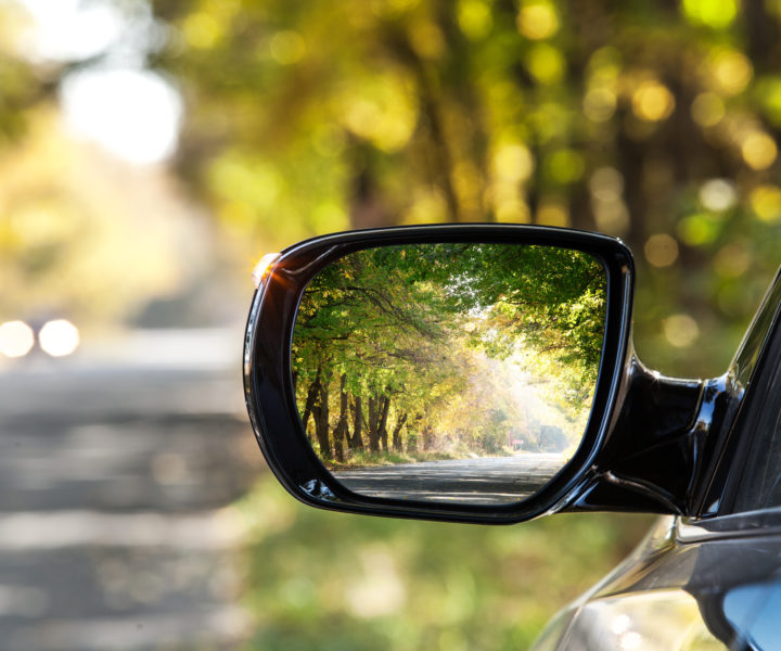 Reflection of sunny autumn road at the car side mirror.