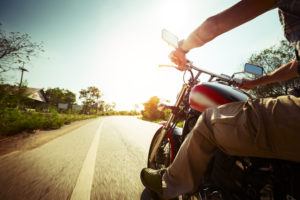 Biker riding motorcycle on an empty road at sunny day