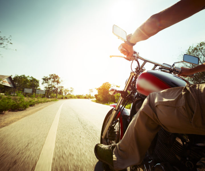 Biker riding motorcycle on an empty road at sunny day